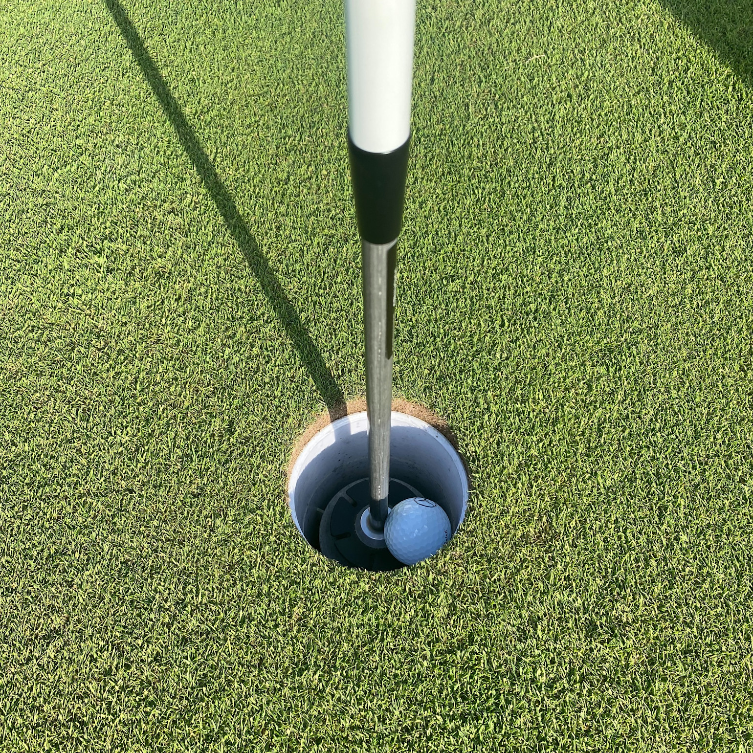 Une balle de golf repose dans le trou à côté du mât du drapeau sur un green bien tondu par temps ensoleillé.