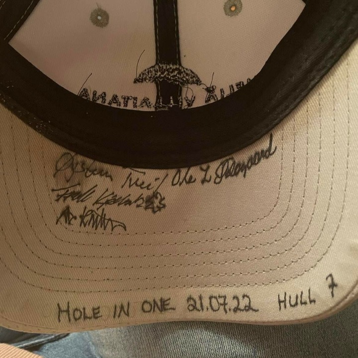 Indersiden af en kasket med flere autografer og teksten "HOLE IN ONE 21.07.22 HUL 7" skrevet på skyggen.