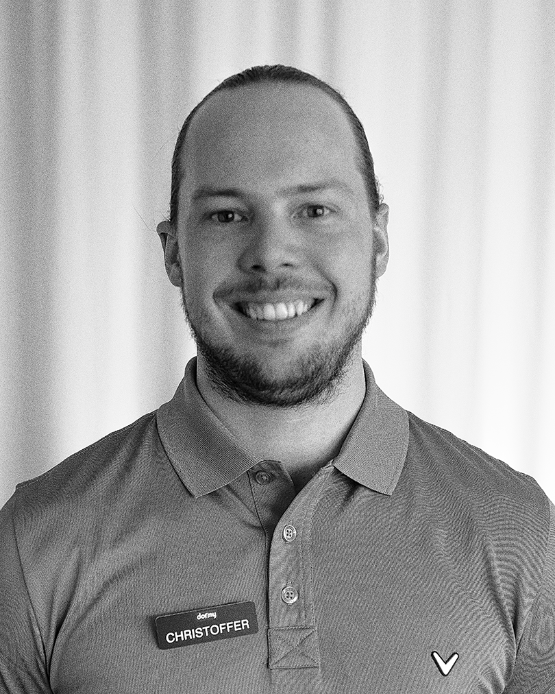 Leende man med hästsvans bär pikétröja och namnbricka med texten "Dormy Christoffer" mot ljus bakgrund.
