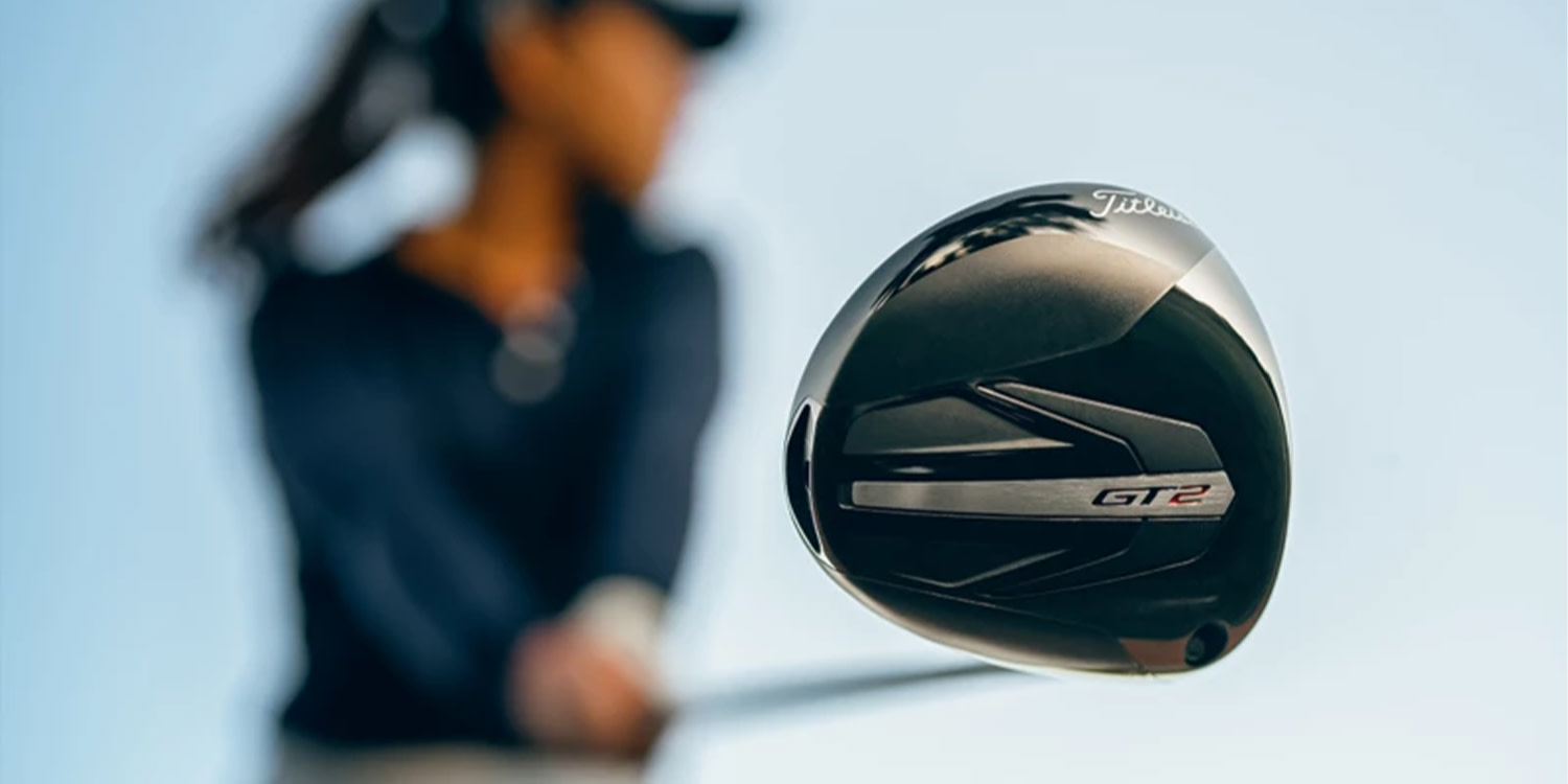 Lähikuva Titleist GT2 -golfmailan lavasta, jota pitää kädessään tummiin pukeutunut henkilö vaaleansinistä taivasta vasten.