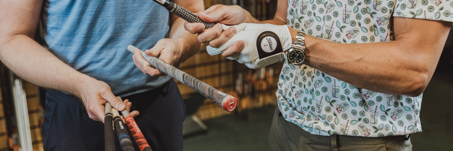 Zwei Personen halten und vergleichen Golfschläger, eine davon trägt einen Golfhandschuh und eine Uhr, in einer Ladenumgebung.