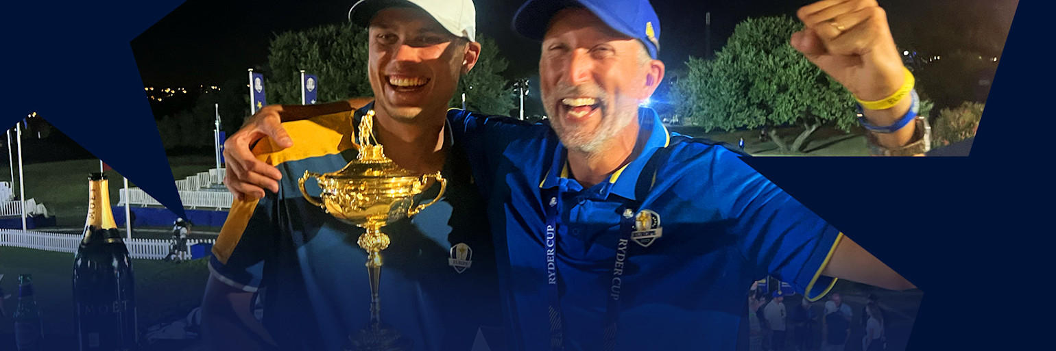 Två glada män i blå Ryder Cup-kläder firar, en håller en guldpokal och den andra höjer näven i segergest utomhus på kvällen.