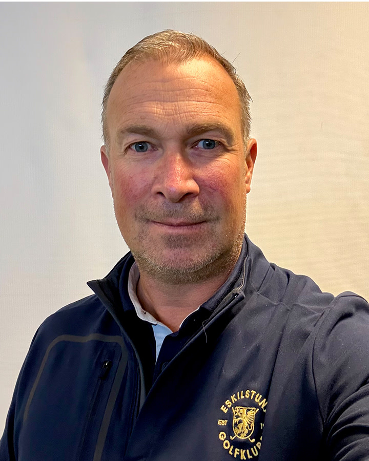 Man ler mot kameran och bär en mörk jacka med Eskilstuna Golfklubb-logotyp, mot en ljus bakgrund.