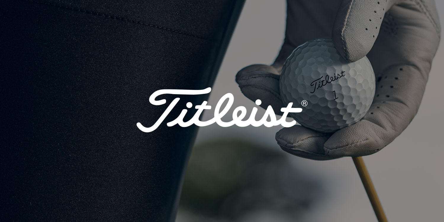 En hånd med golfhandske holder en Titleist-golfbold oven på en tee, med Titleist-logoen i forgrunden.