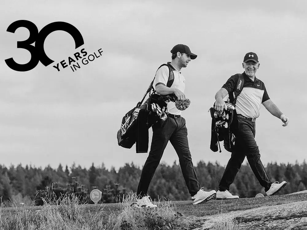 Kaksi golfaria kävelee hymyillen golfkentällä golfbägit mukanaan, ja vasemmassa yläkulmassa näkyy teksti "30 vuotta golfissa".