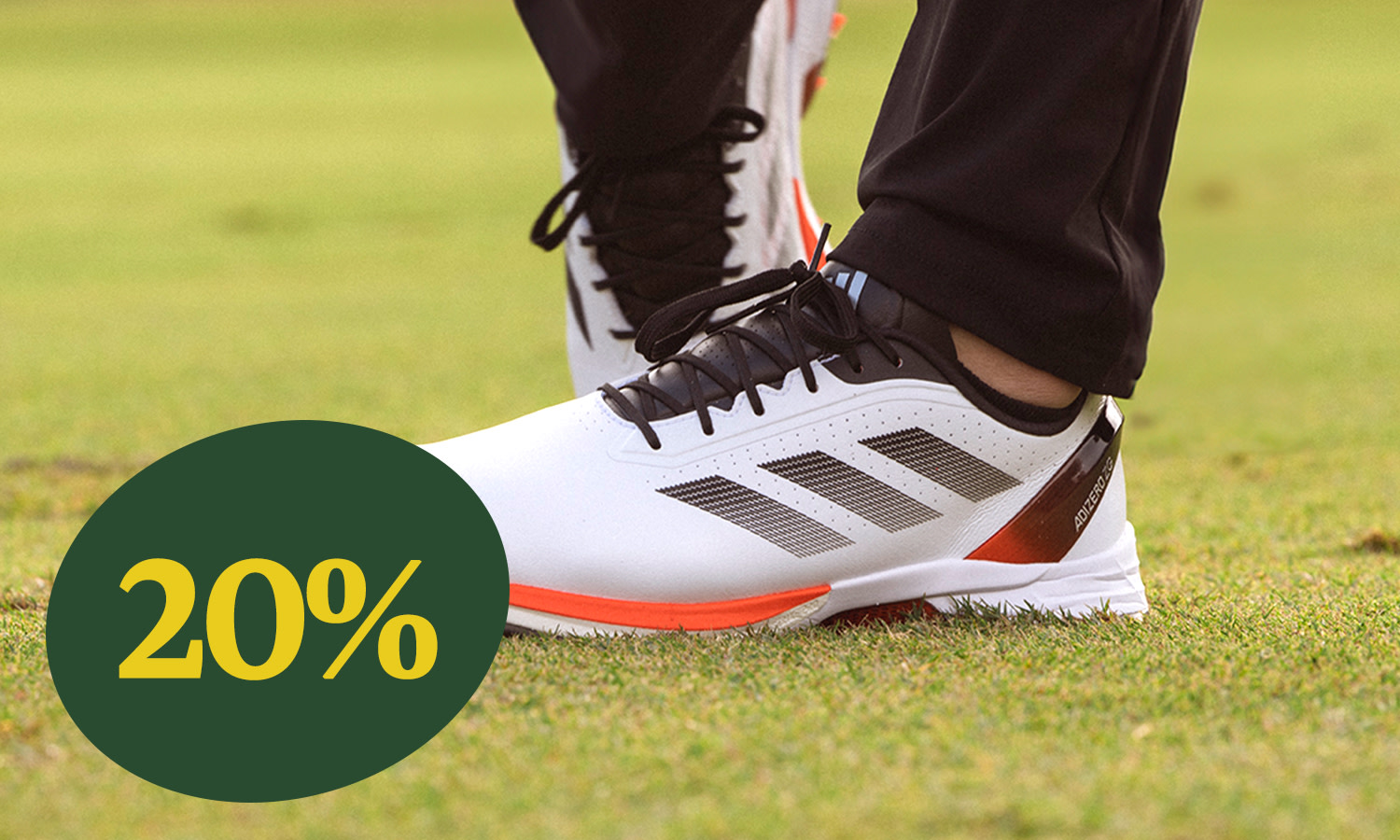 Vita sportskor med svarta ränder används på gräs, med en gul text "20%" i en grön cirkel i förgrunden.