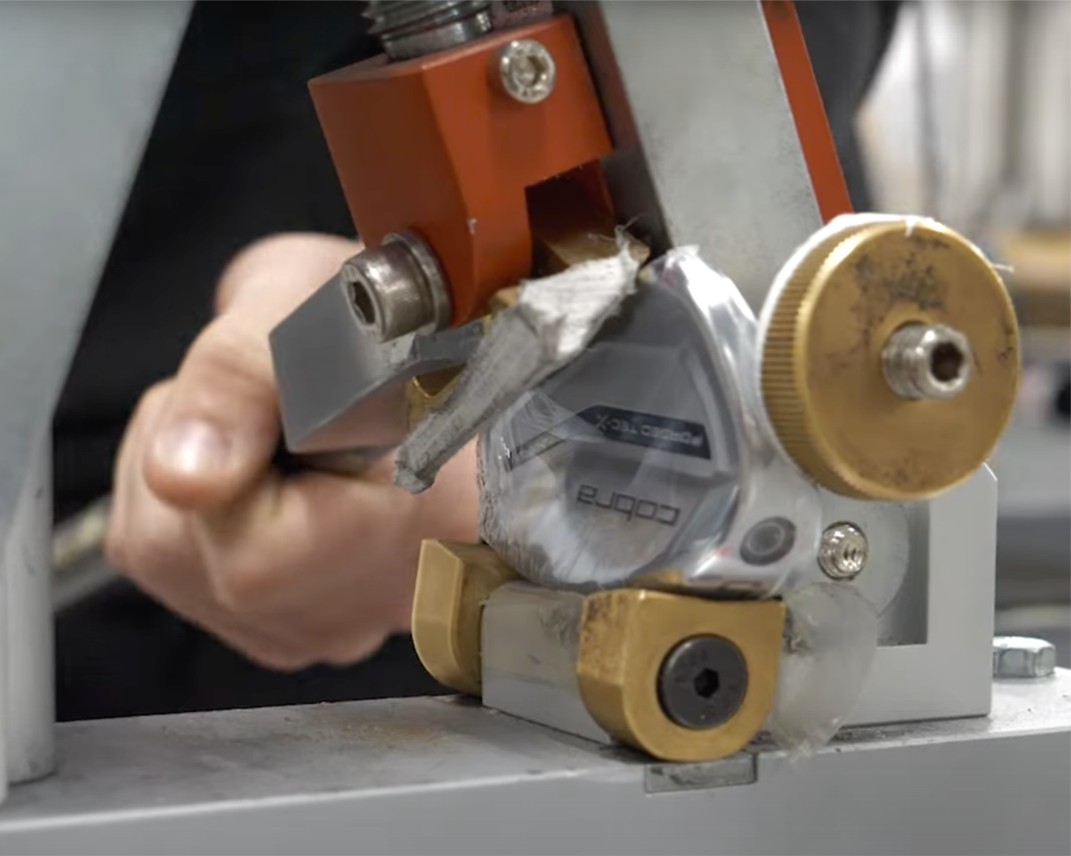 En hand justerar ett golfklubbhuvud av märket Cobra i en metallbearbetningsmaskin i en verkstadsmiljö.