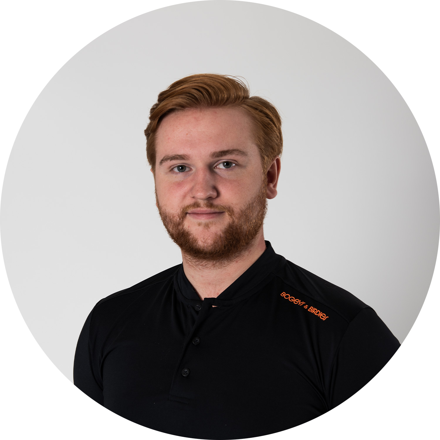 Man med rött hår och skägg bär en svart pikétröja med orange texten "BOGEY & BIRDS" på axeln, mot vit bakgrund.