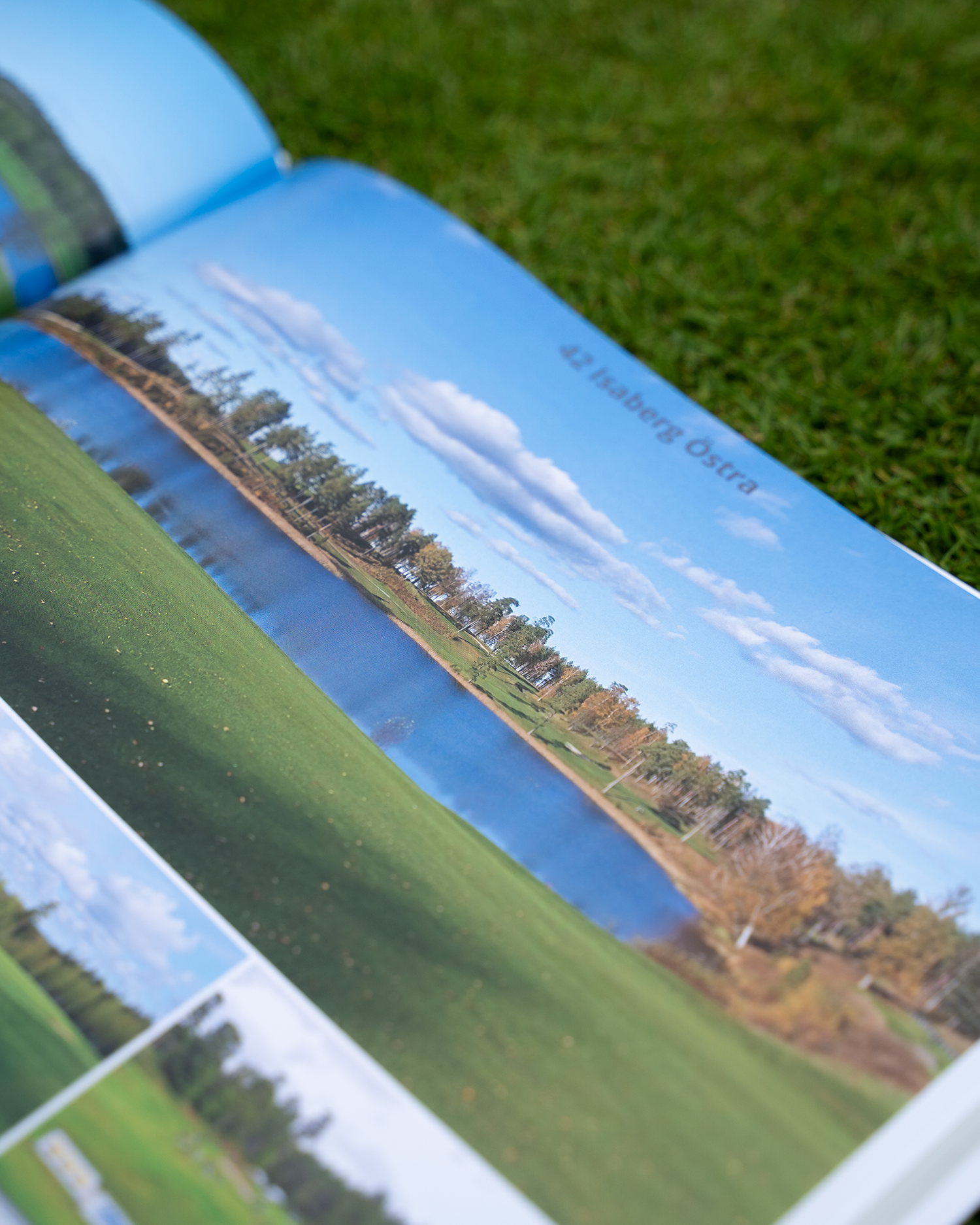 Uppslagen bok visar ett foto av en golfbana med sjö, grönt gräs och träd under blå himmel, texten "42. Isaberg Östra".