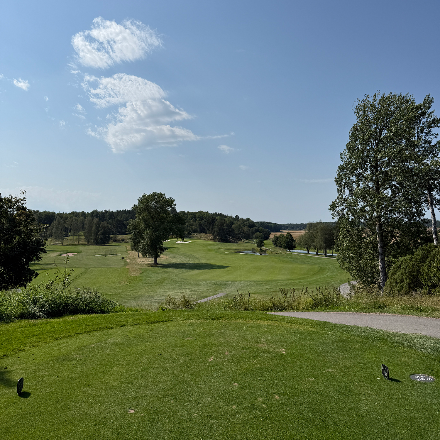 A view over a golf course with green fairways, trees, and a blue sky with a few clouds on a sunny day.
