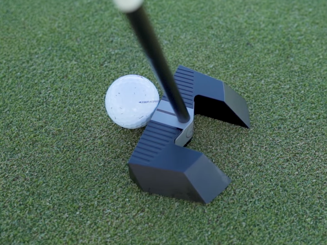 Ein Golfball liegt auf dem Grün neben einem modernen, schwarzen Putterkopf, der bereit ist, den Ball zu schlagen.