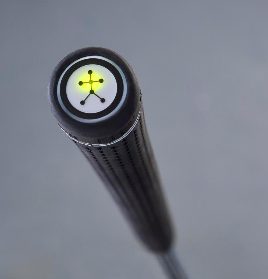 Närbild på toppen av ett golfklubbsgrepp med en lysande gul indikator och ett cirkulärt mönster mot grå bakgrund.