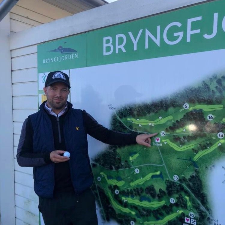 Mand med golfkasket peger på hul 15 på et kort over Bryngfjorden golfbane og holder en golfbold i den anden hånd.