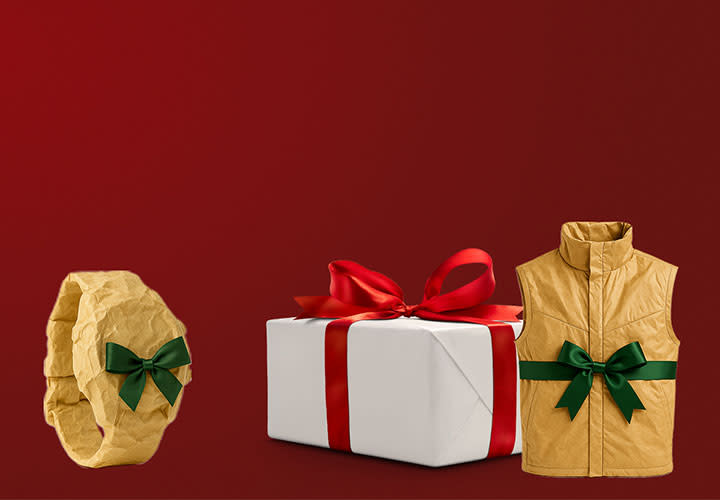 En beige väst och ett beige armband med gröna rosetter står bredvid ett inslaget paket med rött band mot röd bakgrund.