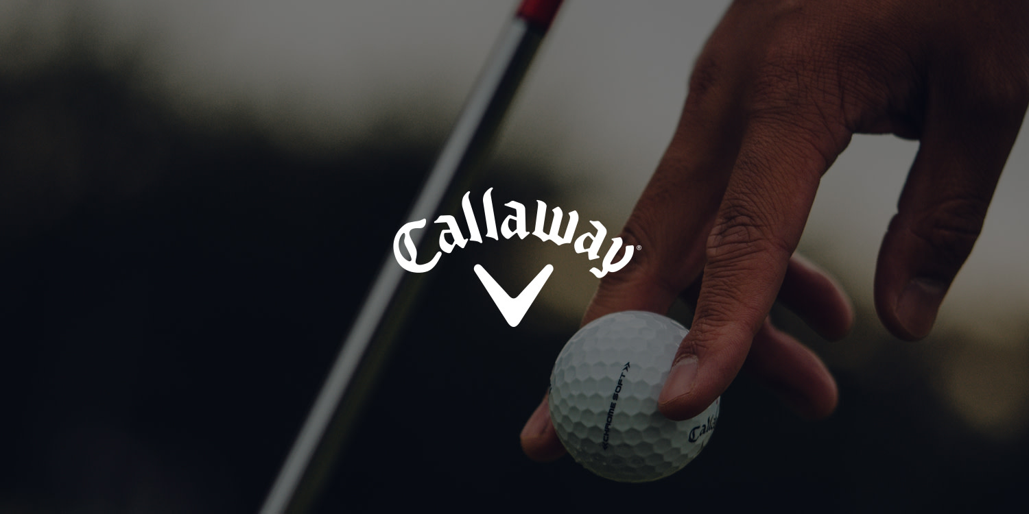 En hånd placerer en Callaway-golfbold på jorden ved siden af en golfkølle, med Callaway-logoet i midten.