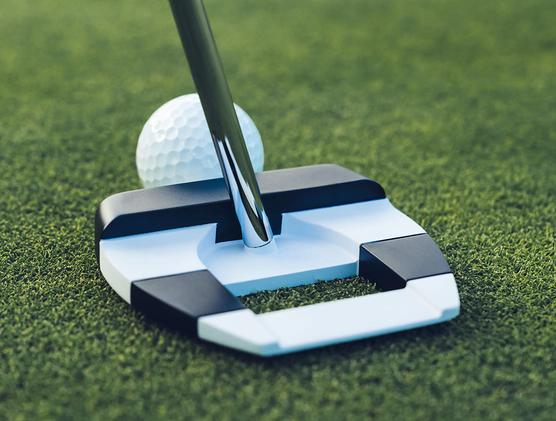 En golfklubba puttar en golfboll på en välklippt grön gräsmatta.