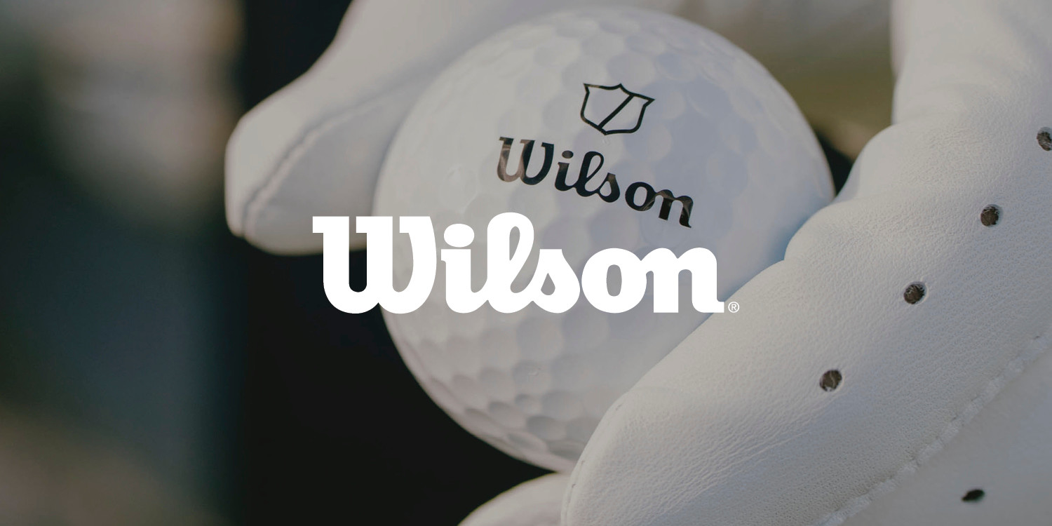 En hvid golfbold med Wilson-logo holdes af en hånd i en hvid golfhandske.