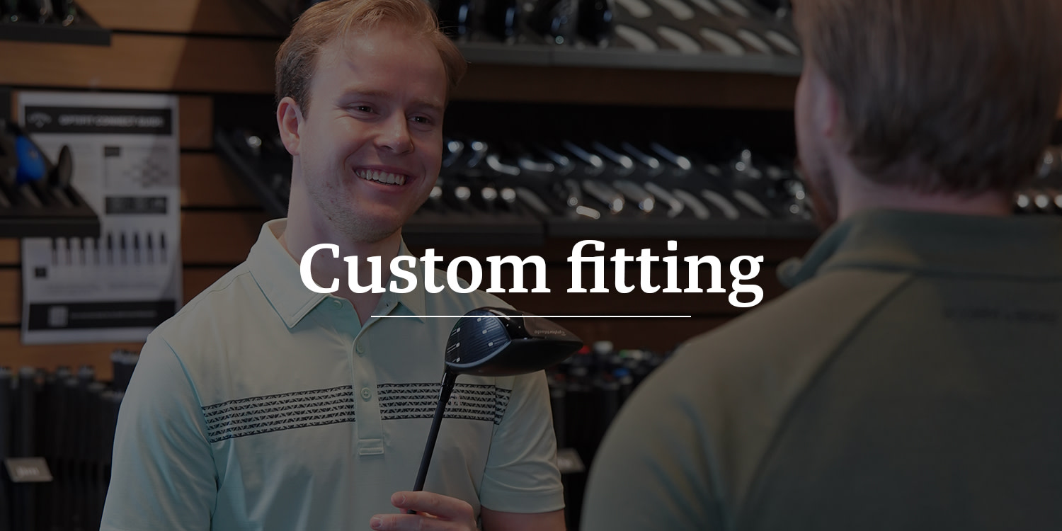 Två män håller i golfklubbor och diskuterar custom fitting i en golfbutik, med texten "Custom fitting" över bilden.