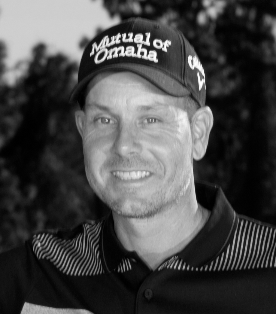 Man med keps med texten "Mutual of Omaha" ler utomhus, klädd i pikétröja med randiga detaljer.