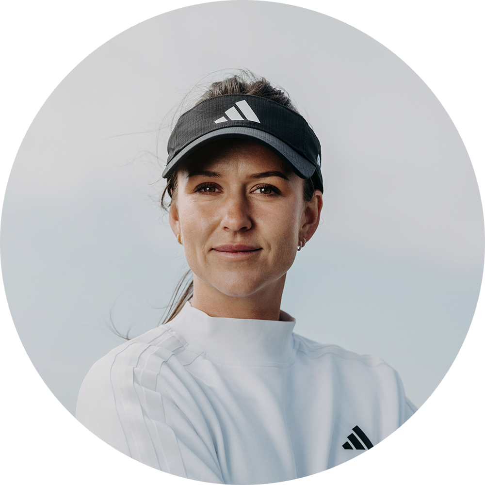 Kvinna med mörk visirkeps och vit Adidas-tröja står utomhus och tittar lugnt mot kameran.