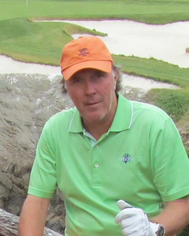 Man med orange keps och grön pikétröja står utomhus på en golfbana, håller en golfhandske och tittar mot kameran.