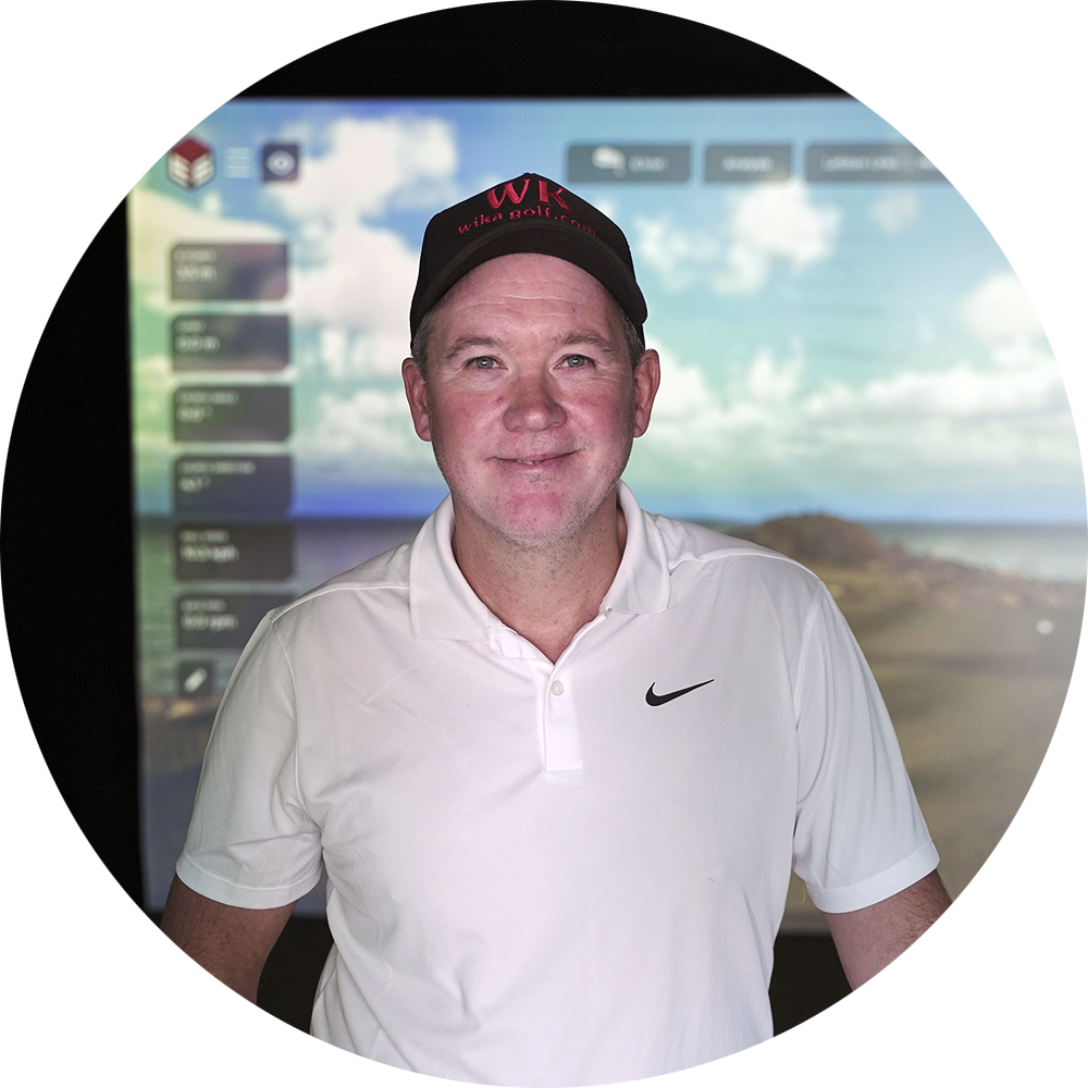 Mann mit weißem Poloshirt und schwarzer Kappe mit der Aufschrift „Wika Golf“ steht vor einem Golfsimulator mit Landschaftshintergrund.