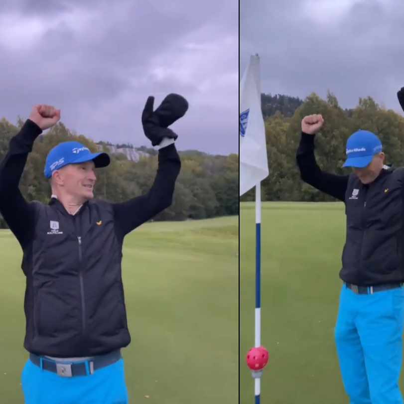 Mand i blå kasket og blå bukser fejrer med armene i vejret på en golfbane ved siden af en flagstang.