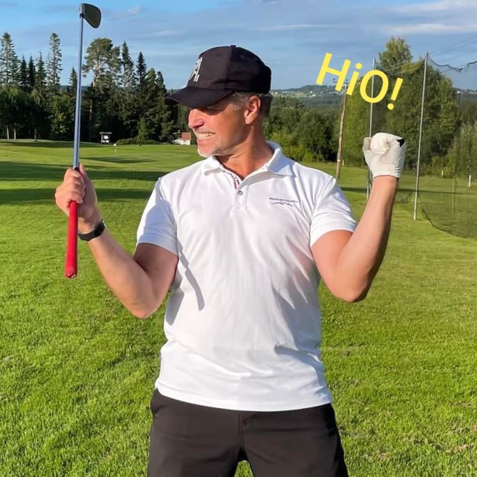 Mand i hvid polo og sort kasket fejrer med en golfkølle på en grøn golfbane, teksten "HiO!" ses i gult over ham.