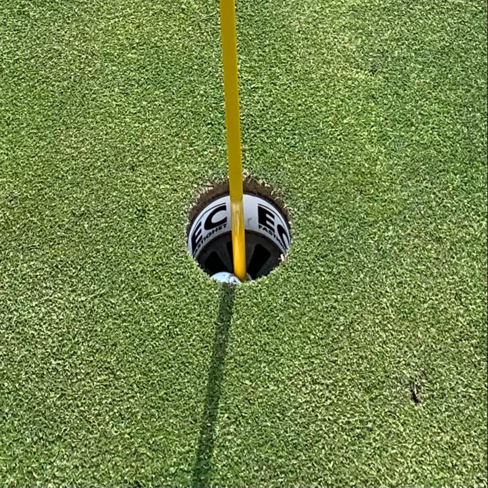 Golfbold ligger i hullet ved siden af en gul flagstang på en velplejet green.