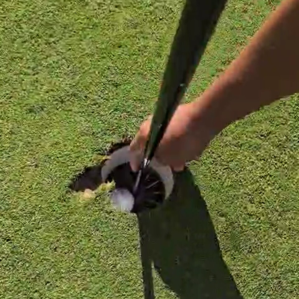En hand tar upp en golfboll ur hålet på en golfbana med flaggstången kvar i koppen.