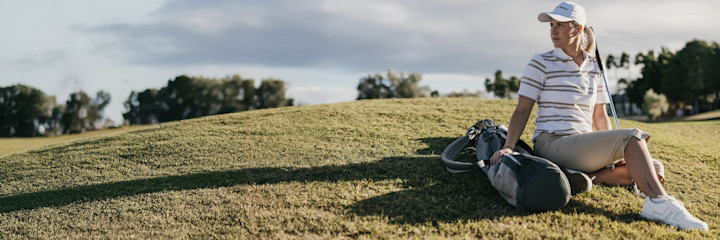 Kaksi naista kävelee yhdessä golfkentällä, molemmilla on yllään urheiluvaatteet ja he pitävät golfmailoja käsissään.